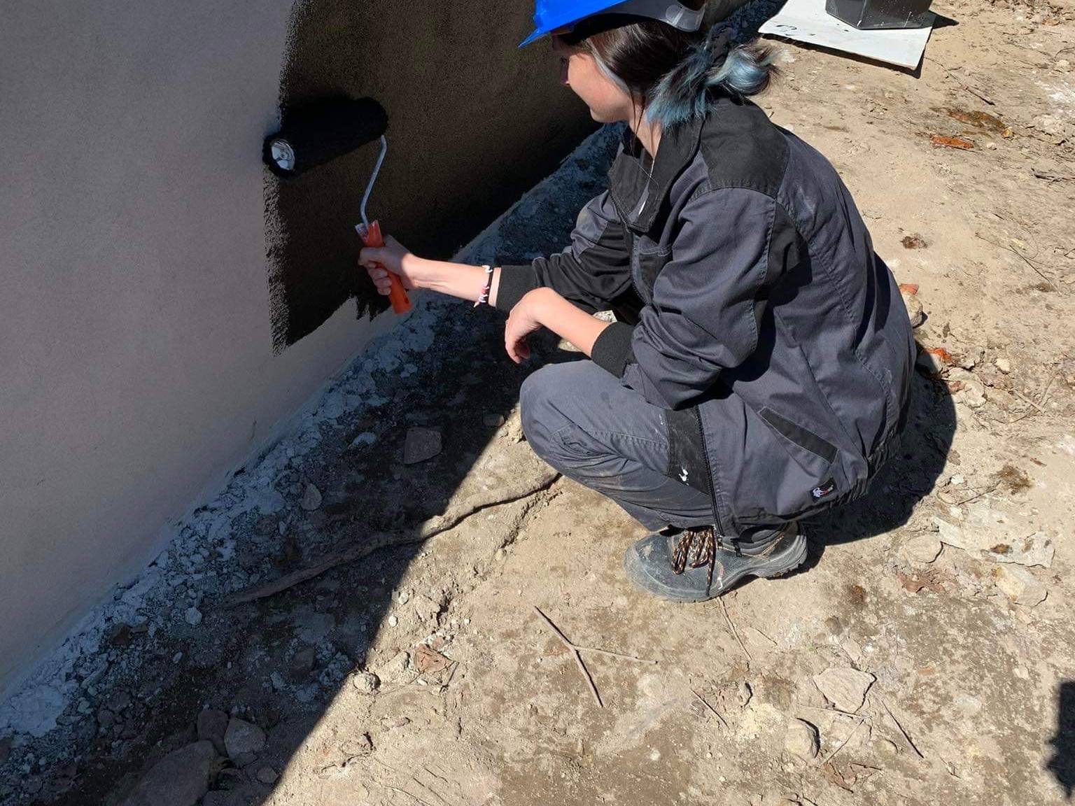 Trainee with a helmet painting a wall on a building site