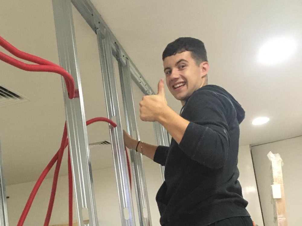 Trainee building a drywall frame, giving a thumbs up